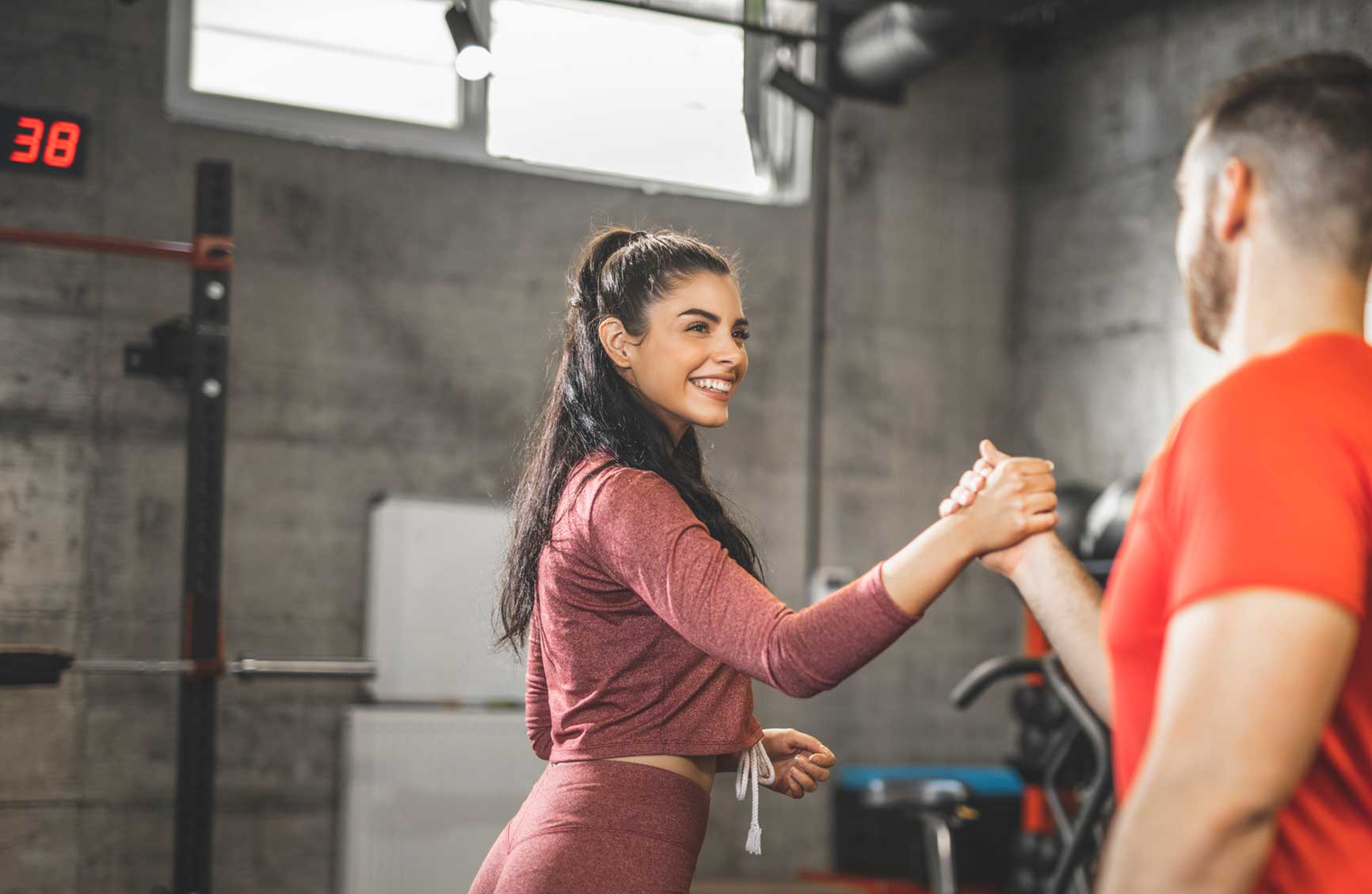 Young woman and man shaking hands after an intense training session in the gym, focus on woman.