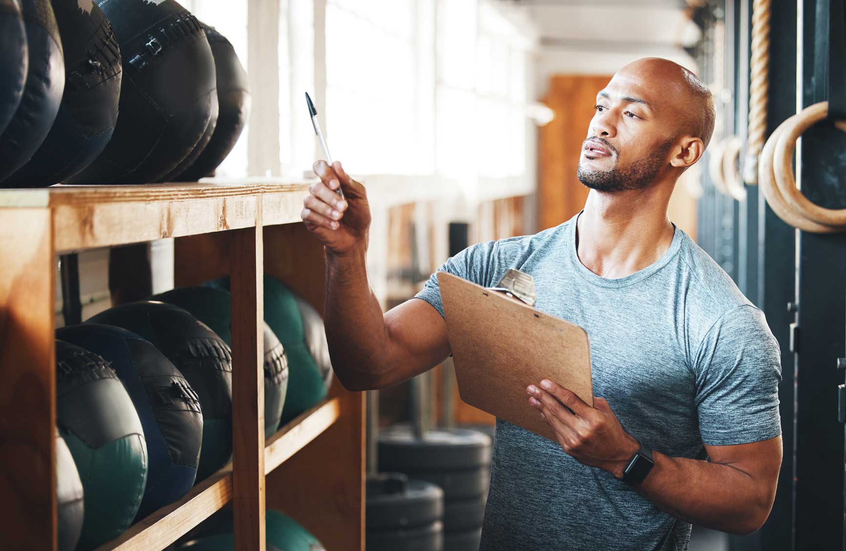 Shot of a muscular young man using a clipboard while checking equipment in a gym.