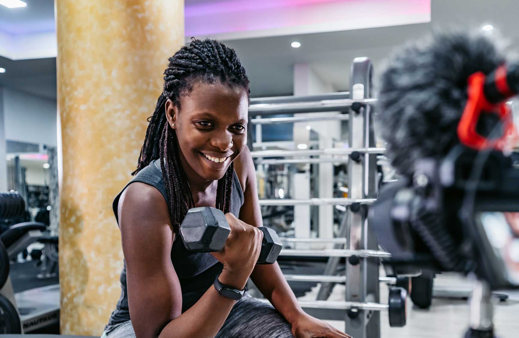 Smiling fitness influencer filming a workout video with dumbbells at the gym