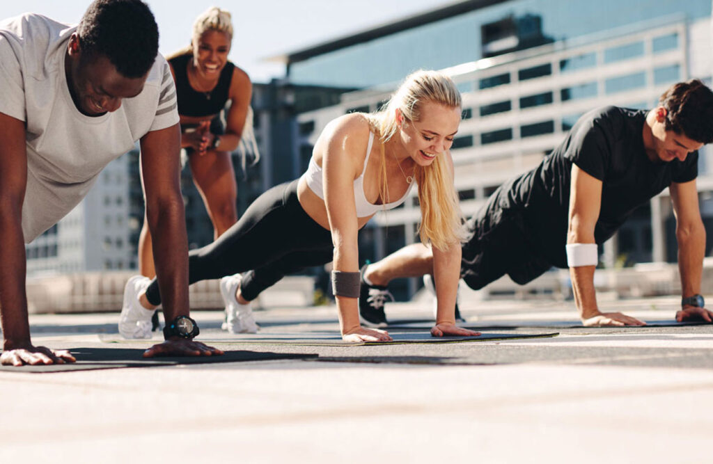 Group of people doing outdoor push-up exercises together on mats during a workout session.