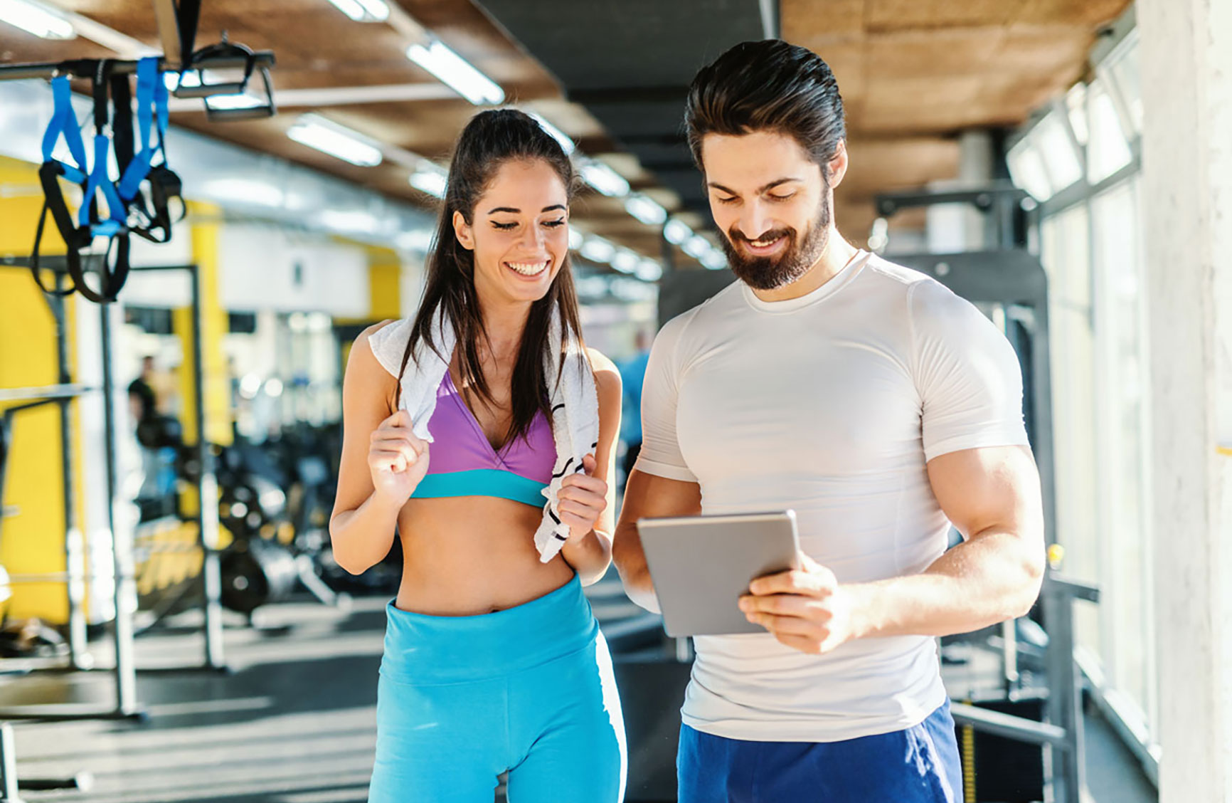 Man holding a tablet and discussing workout plans with a woman in a gym, both smiling.