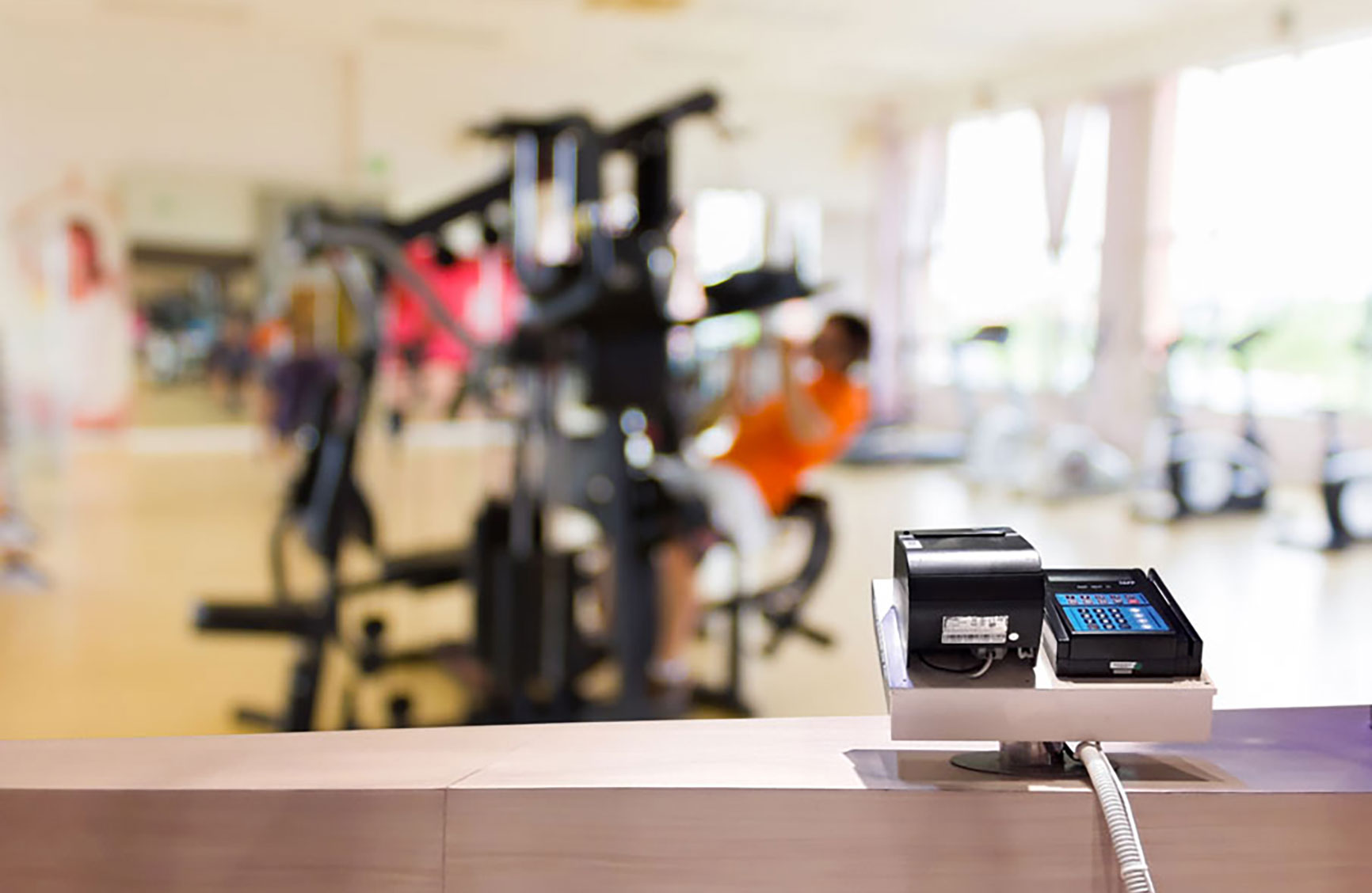 Payment terminal at a gym front desk with fitness equipment in the background.